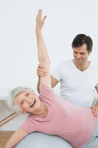 Physical therapist assisting senior woman with yoga ball — Stock Photo, Image