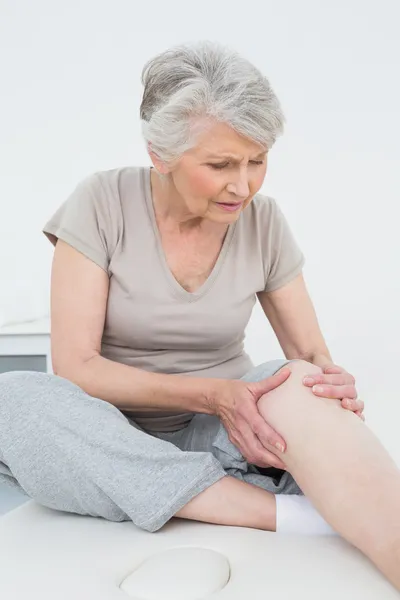 Senior vrouw met haar handen op een pijnlijke knie Stockfoto