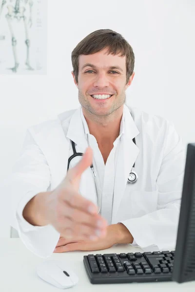 Médico masculino oferecendo um aperto de mão na mesa do consultório médico Imagem De Stock