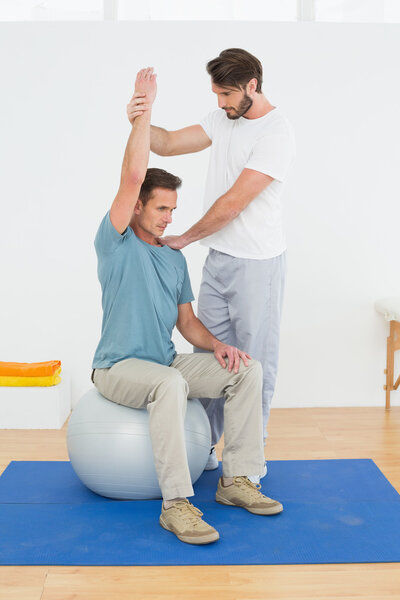 Man on yoga ball working with a physical therapist Stock Picture