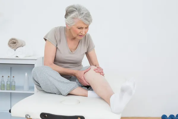 Äldre kvinna med händerna på en smärtsam knä Royaltyfria Stockbilder