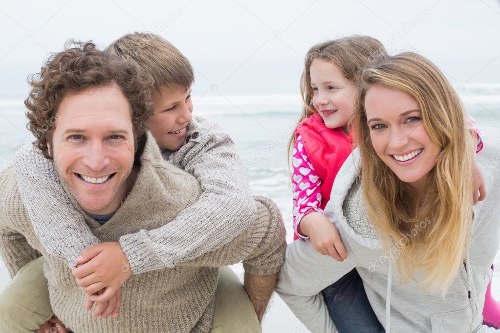 Happy couple piggybacking kids at beach