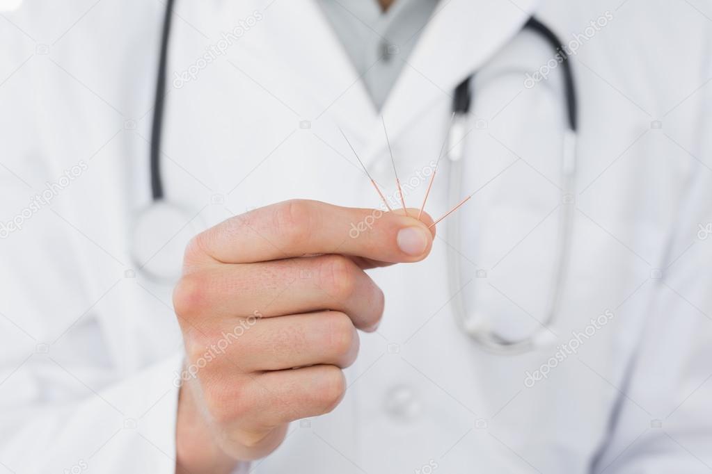 Mid section of a male doctor holding acupuncture needles