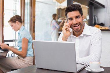 mutlu bir adam kafede dizüstü bilgisayar ve cep telefonu kullanma