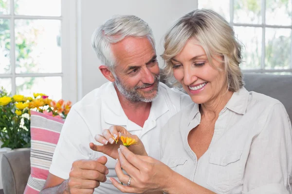 Glückliches älteres Paar mit einer Blume im Wohnzimmer — Stockfoto