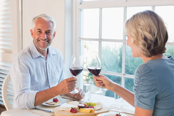 Portrait of a mature couple toasting wine glasses over food — Stock Photo, Image