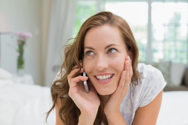 Hermosa mujer joven sonriente usando el teléfono móvil en la cama — Foto de Stock