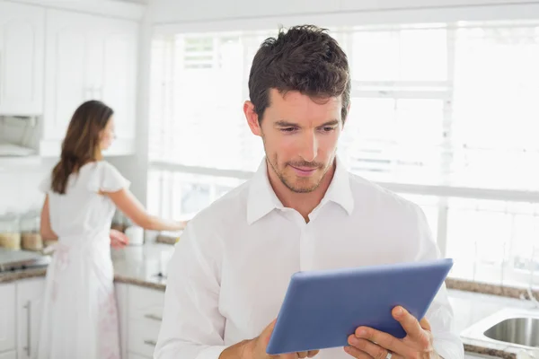 Homem usando tablet digital com mulher no fundo na cozinha — Fotografia de Stock