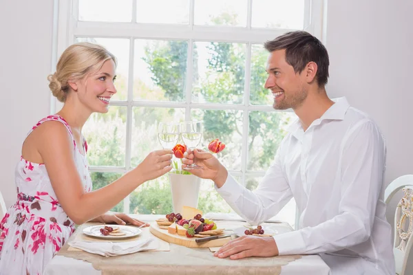 Feliz joven pareja tostando copas de vino sobre la comida — Foto de Stock