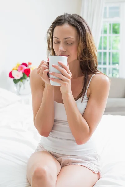 Avslappnad kvinna med kaffekopp sitter i sängen — Stockfoto