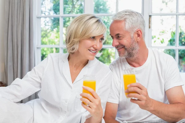 Casal maduro segurando sucos de laranja em casa — Fotografia de Stock