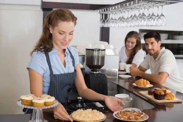 Cafe owner holding sweet snacks with couple at counter in coffee — Stock Photo, Image