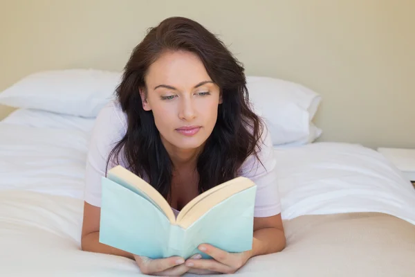 Женщина читает книгу, когда лежит в постели — стоковое фото