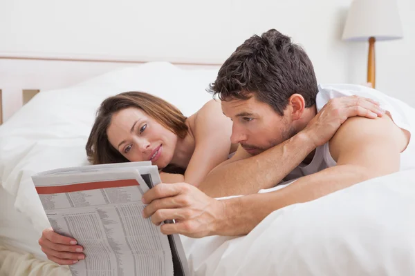 Пара читающих газету вместе в постели — стоковое фото
