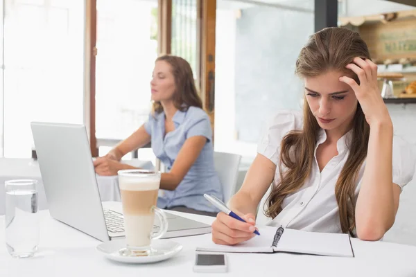 Mulher concentrada escrevendo notas com laptop no café — Fotografia de Stock