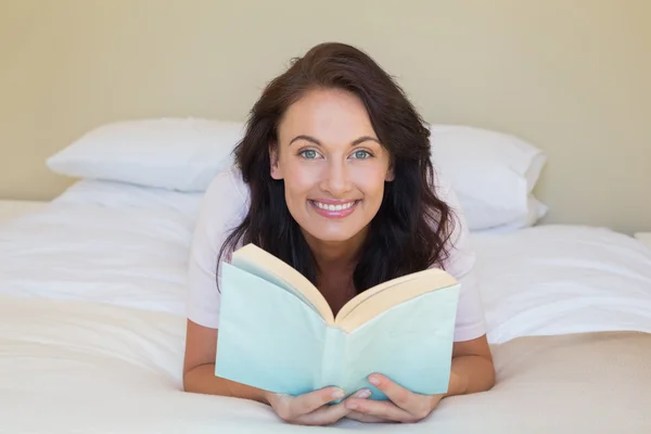 Woman holding book while lying in bed — Stock Photo, Image