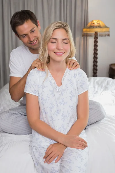 Smiling man massaging woman's shoulders in bed — Stock Photo, Image