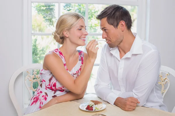 Loving young woman feeding man pastry at home — Stock Photo, Image