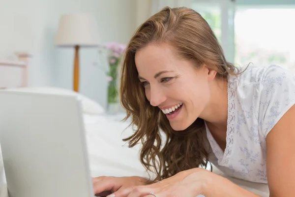 在床上用笔记本电脑微笑的年轻女人 — 图库照片