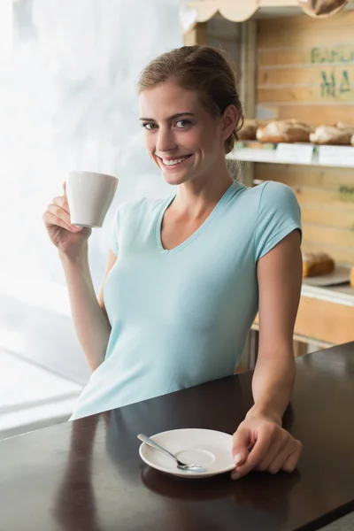 Smiling woman drinking coffee at counter in coffee shop — Stock Photo, Image