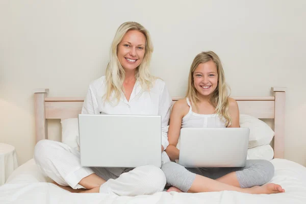 Feliz madre e hija usando computadoras portátiles en la cama — Foto de Stock