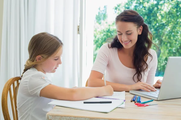 Mother looking at daughter doing homework at table — Stock Photo, Image