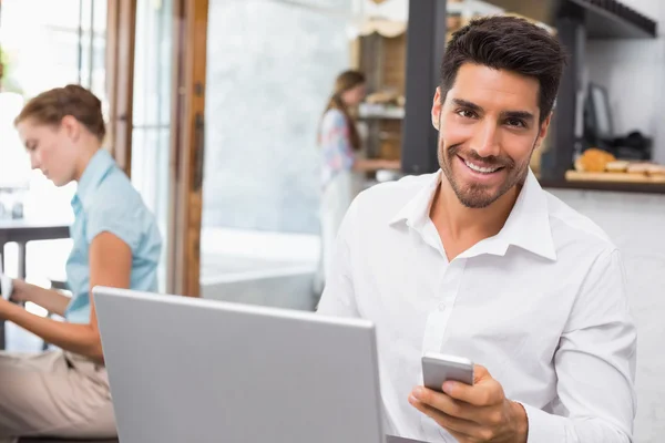 kafede dizüstü bilgisayar ve cep telefonu kullanan adam