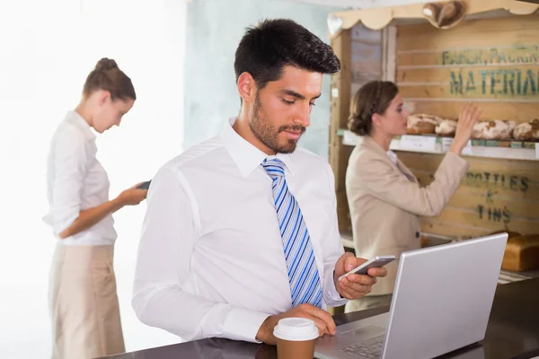 Businessman using mobile phone and laptop in office cafeteria — Stock Photo, Image