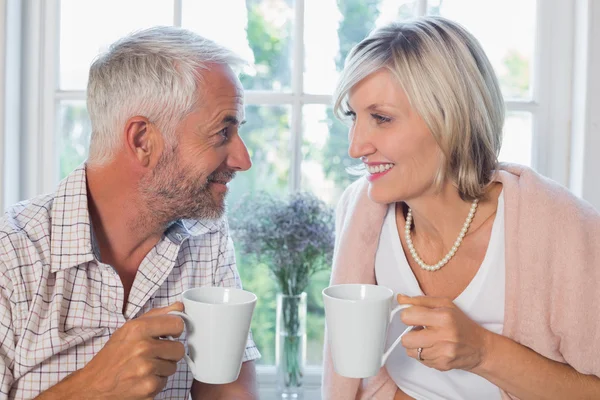 Smiling mature couple with coffee cups at home — Stock Photo, Image