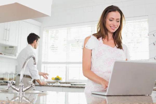 Woman using laptop with man in background in kitchen — Stock Photo, Image