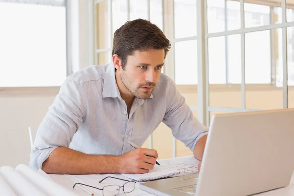 Businessman working on blueprints and laptop in office — Stock Photo, Image
