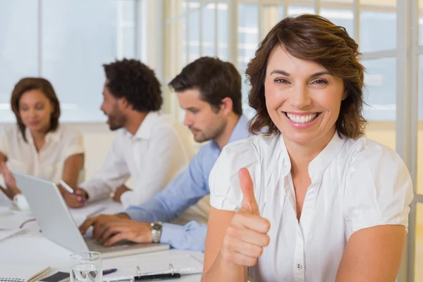 Mujer de negocios sonriente haciendo gestos con los pulgares hacia arriba con colegas —  Fotos de Stock