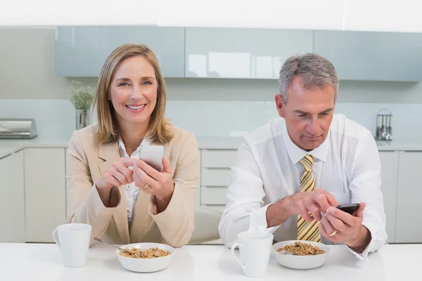 Mensagens de texto de casal de negócios enquanto toma café da manhã na cozinha — Fotografia de Stock