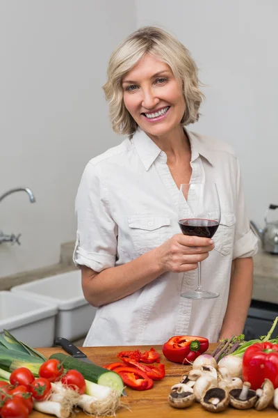 Happy mature woman with vegetables and wine glass in kitchen — Stock Photo, Image