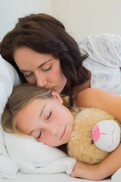 Mother kissing sleeping daughter in bed — Stock Photo, Image