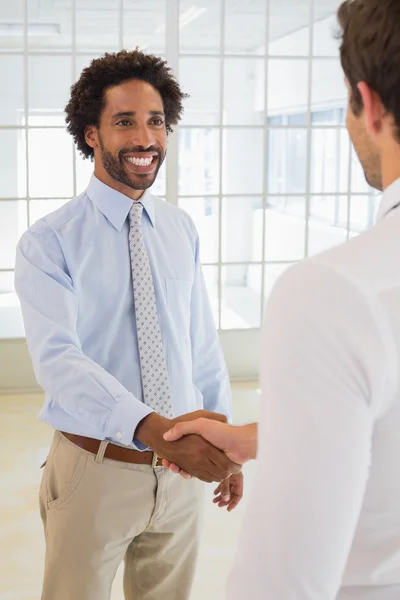 Smiling young businessmen shaking hands in office — Stock Photo, Image