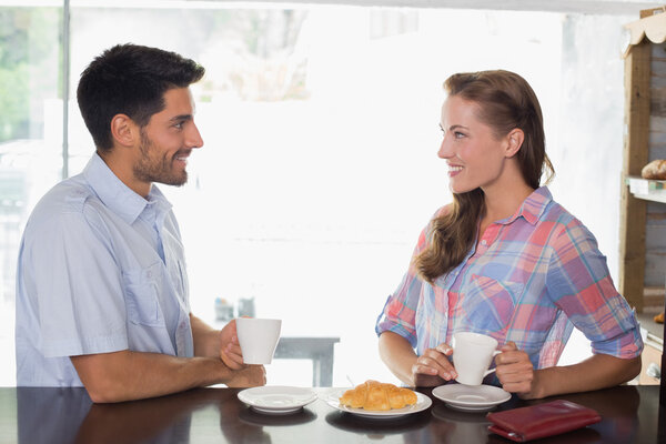 Smiling couple with coffee and croissant at coffee shop