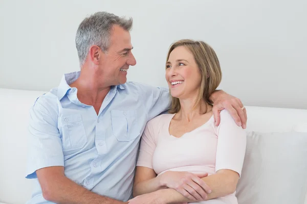 Relaxed couple sitting on sofa with arm around — Stock Photo, Image