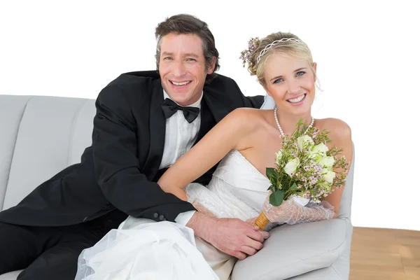 Bride and groom with flower bouquet sitting on sofa — Stock Photo, Image