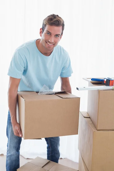 Uomo sorridente con scatole di cartone nella nuova casa — Foto Stock