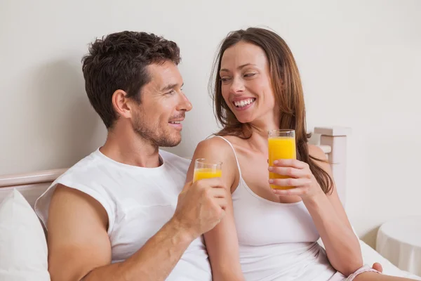 Happy relaxed couple with orange juices in bed — Stock Photo, Image