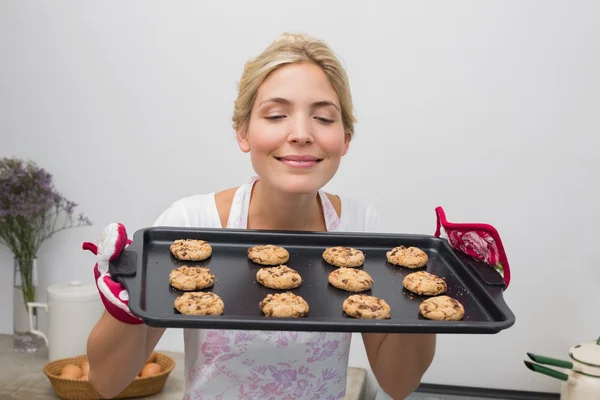 Woman holding a tray of cookies with eyes closed in kitchen — Stock Photo, Image