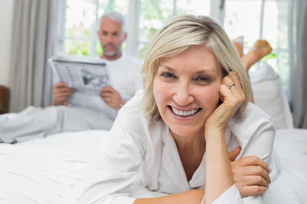 Lachende vrouw met man leest de krant in bed — Stockfoto