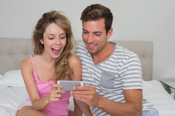 Веселая пара читает текстовые сообщения в постели — стоковое фото