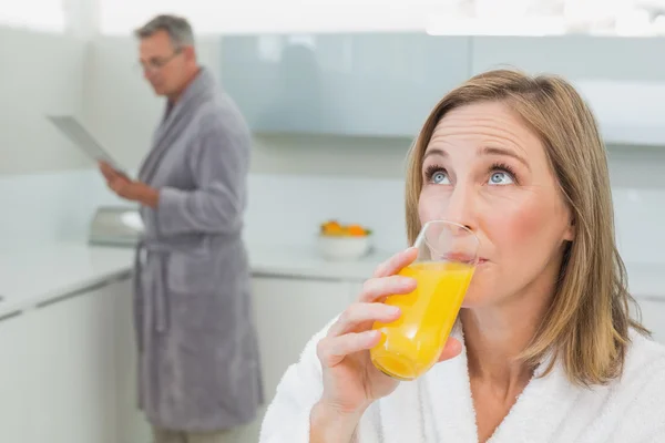 Mujer bebiendo jugo de naranja con el hombre de fondo —  Fotos de Stock