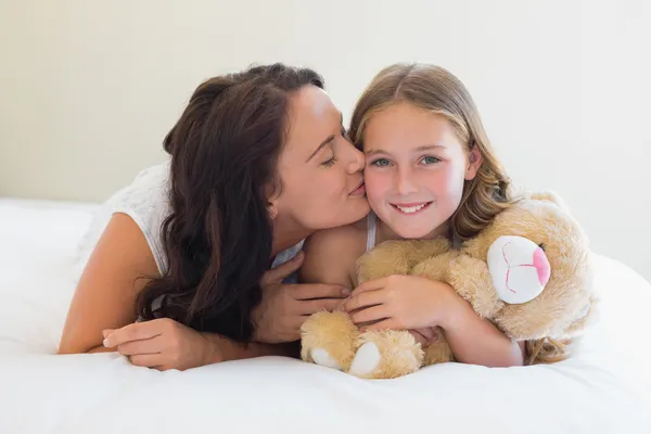 Flicka får puss från mamma i sängen — Stockfoto