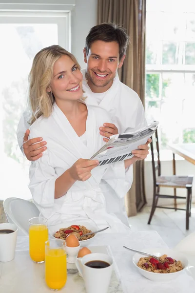 Happy couple reading newspaper while having breakfast at home — Stock Photo, Image