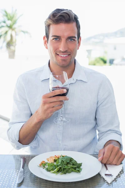 Jovem sorridente com copo de vinho tendo comida — Fotografia de Stock