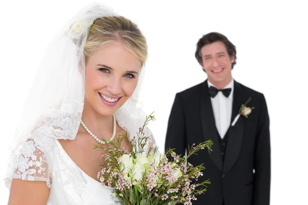 Braut hält Strauß, während Bräutigam im Hintergrund steht — Stockfoto