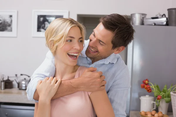 Cheerful man embracing woman from behind in kitchen — Stock Photo, Image
